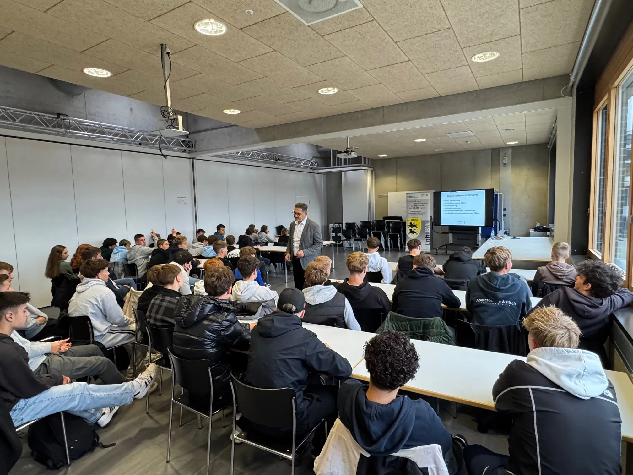 Schüler sitzen in einem Raum und hören dem Vorstand der LohiBW zu.